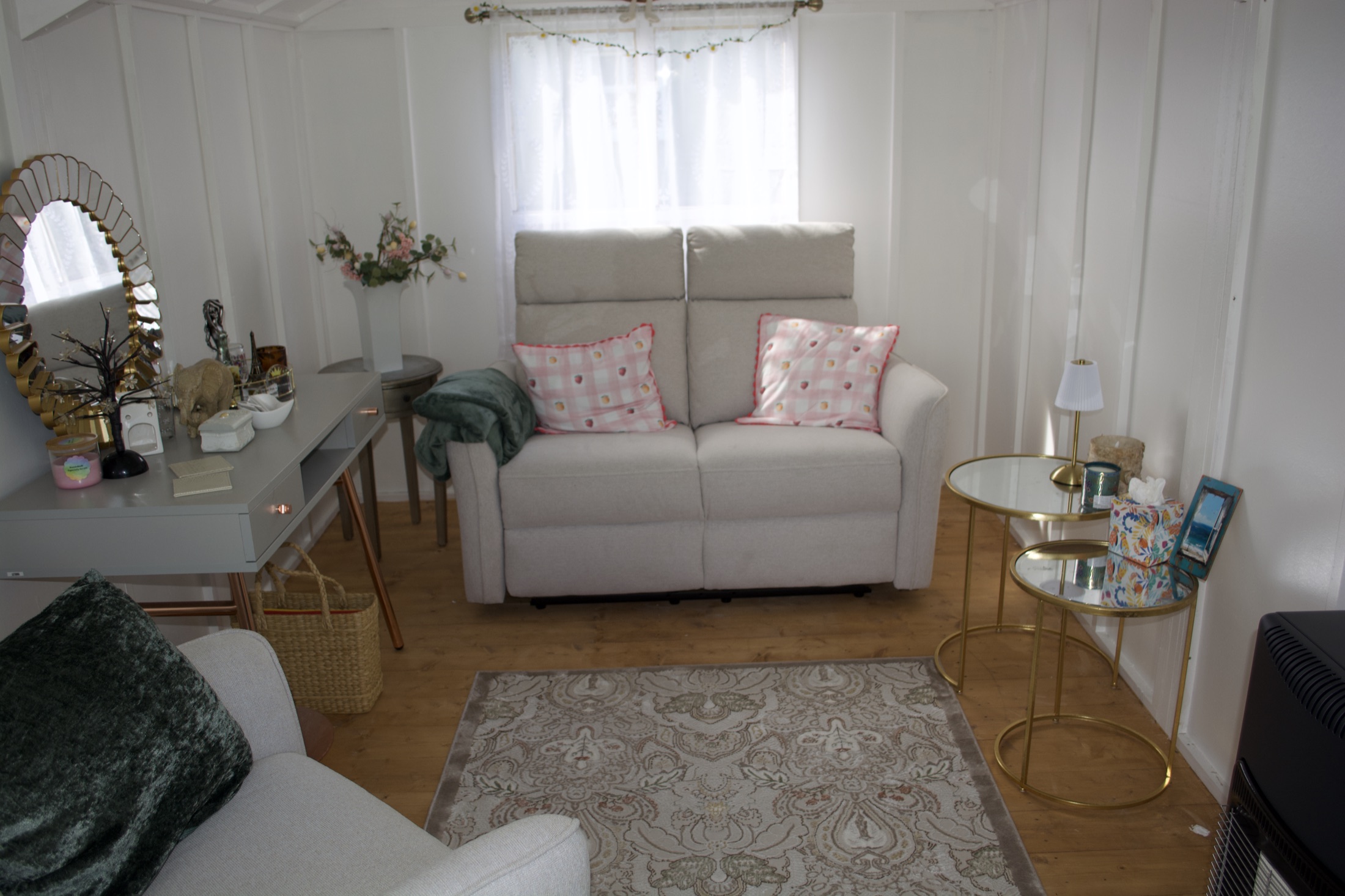 Cabin interior with a light-grey sofa and armchair, patterned rug, side tables and curtained window